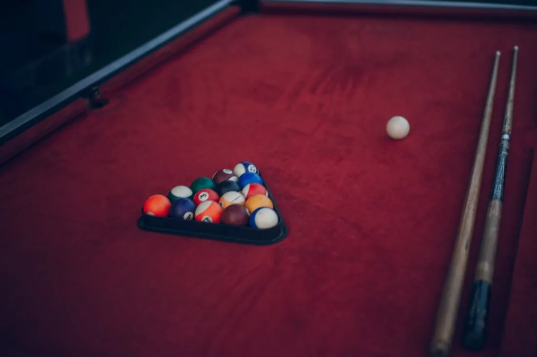 Billardtisch mit grüner Spielfläche und Queues an der Wand