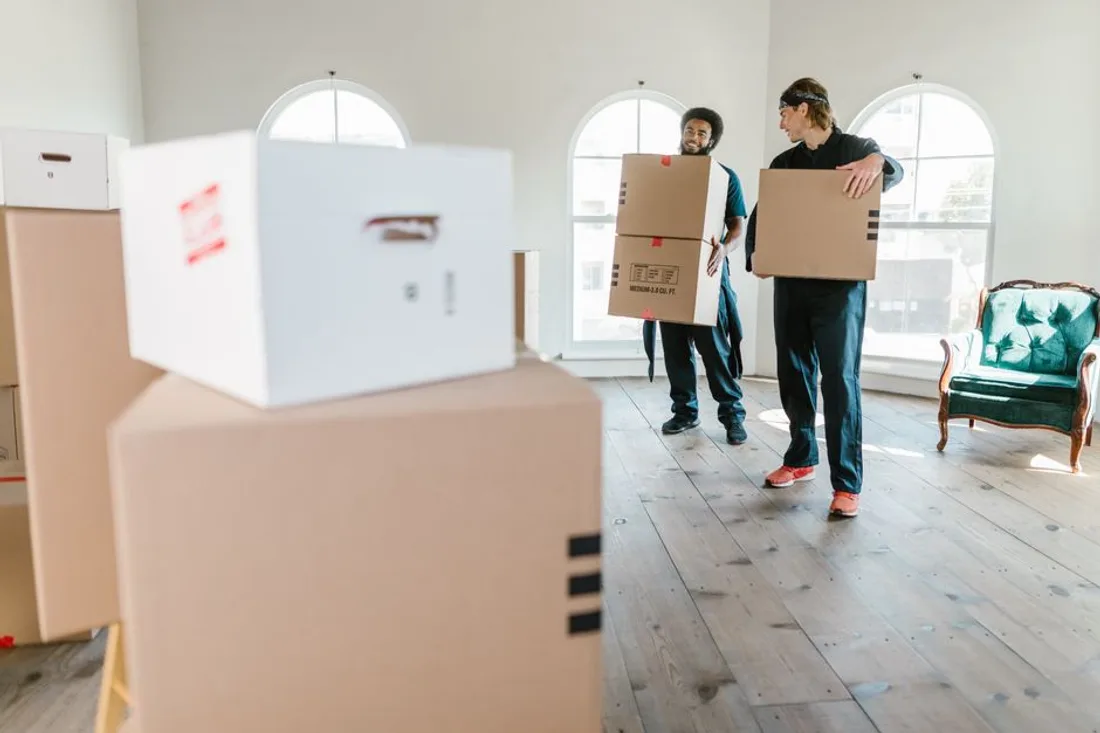 Zwei Umzugshelfer tragen Umzugskartons durch einen hellen, leeren Raum